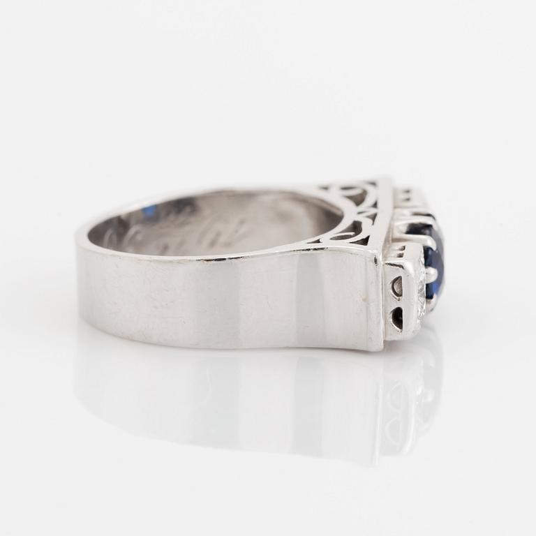 An 18K white gold ring set with a faceted sapphire, possibly synthetic, and round brilliant-cut diamonds.