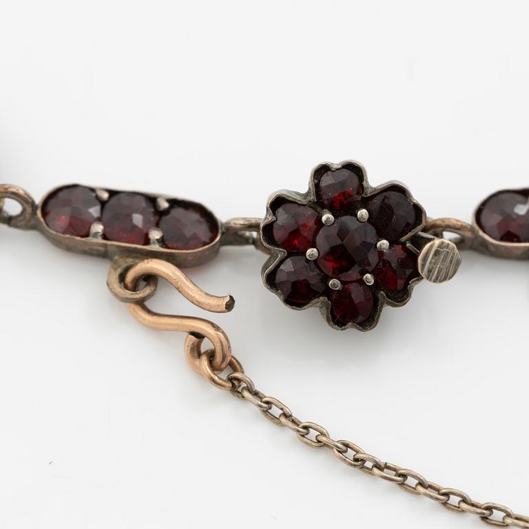 Garniture, necklace/bracelet and earrings in silver with garnets in the form of floral motifs, around the turn of the 20th century.