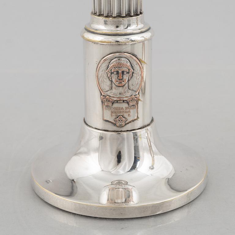 A pair of candlesticks and a commemorative pin from the Olympic Games in Stockholm 1912.