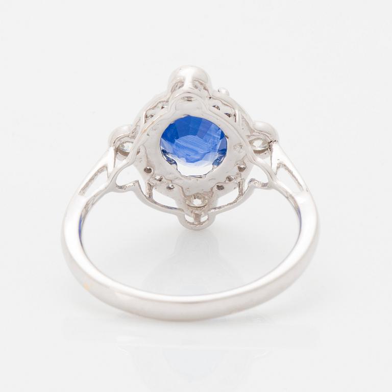 An 18K white gold ring set with a faceted sapphire and round brilliant-cut diamonds.