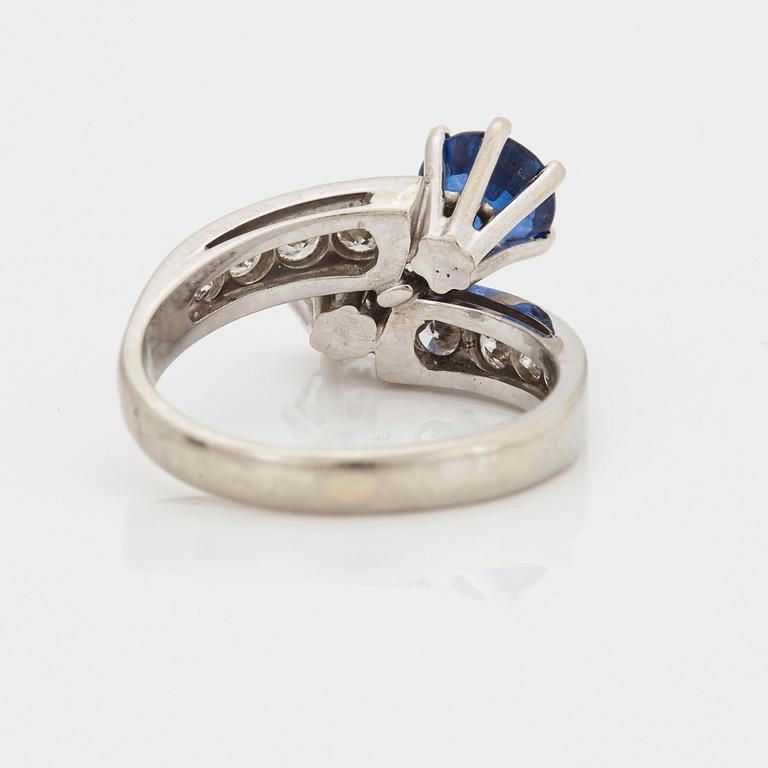 A CROSS-OVER RING set with a round mixed-cut sapphire and round brilliant-cut diamonds.