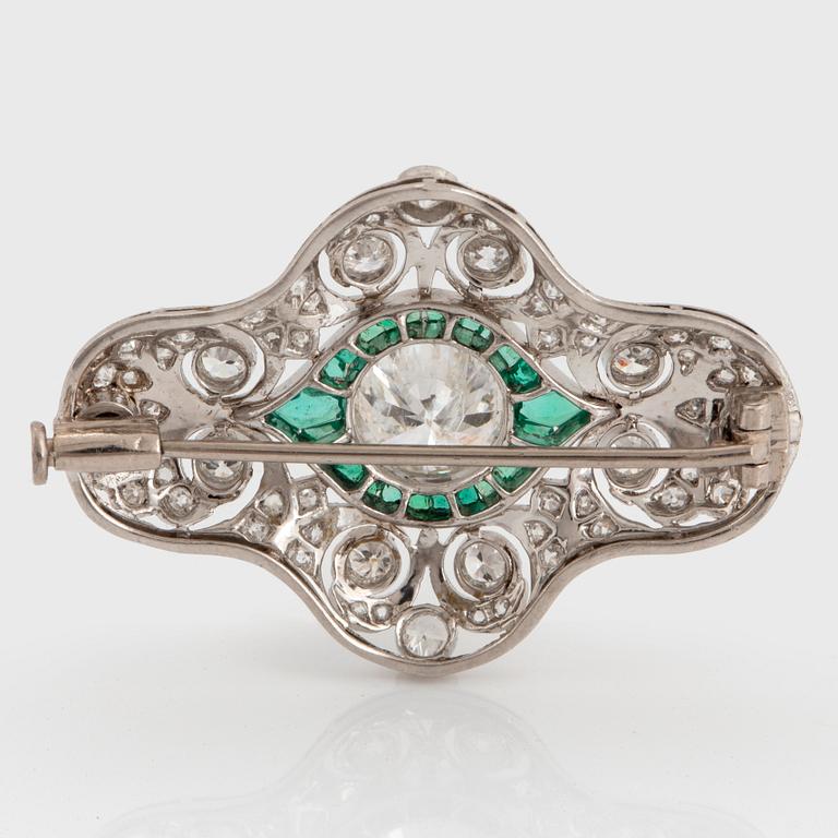 A platinum brooch set with round brilliant- and old-cut diamonds and faceted emeralds.