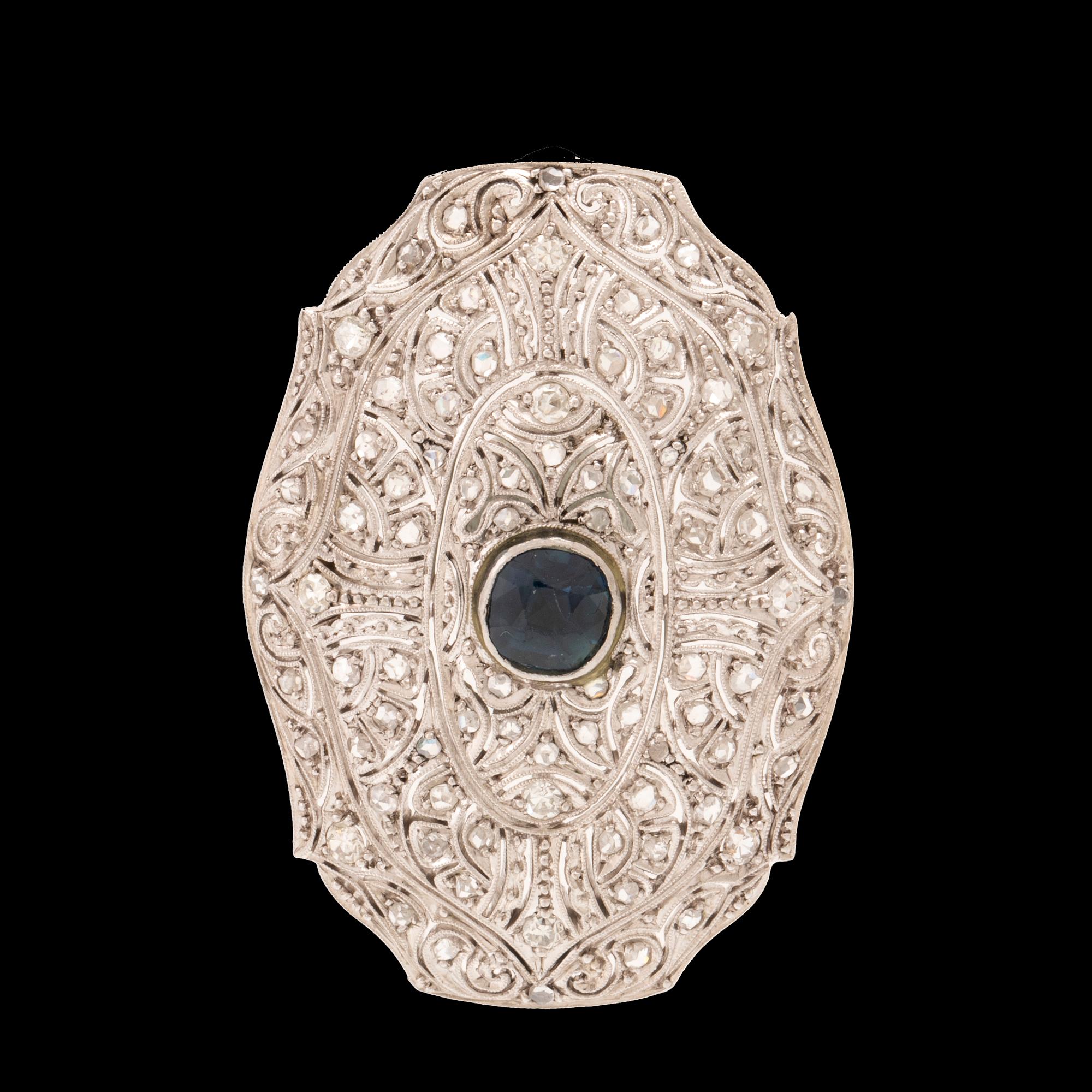 An 18K white gold brooch set with a facet-cut sapphire possibly synthetic, as well as brilliant and rose-cut diamonds.
