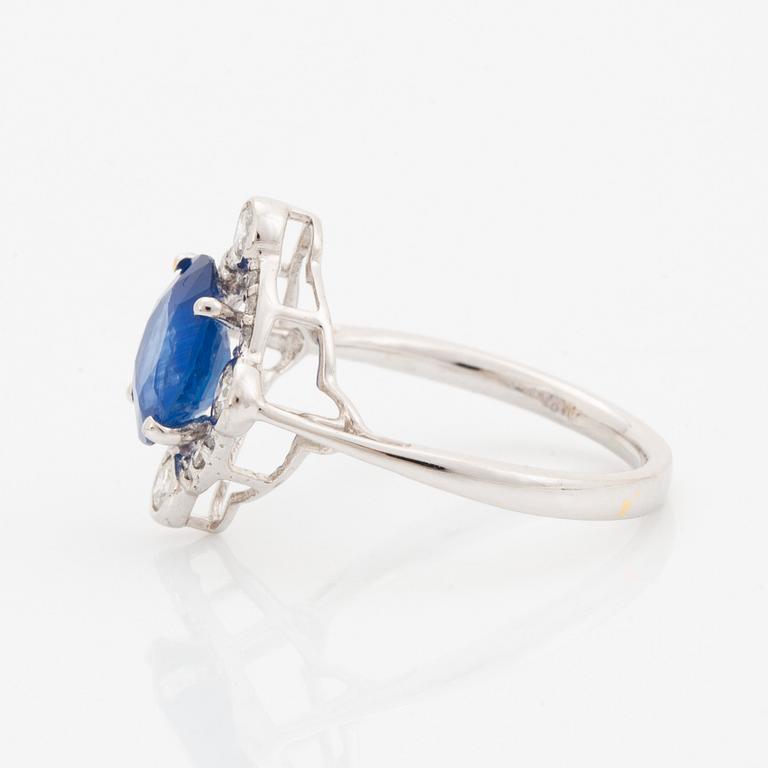 An 18K white gold ring set with a faceted sapphire and round brilliant-cut diamonds.