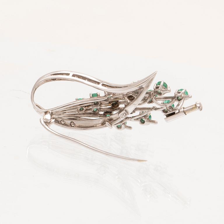 An 18K white gold brooch with round brilliant cut emeralds and single cut diamonds.