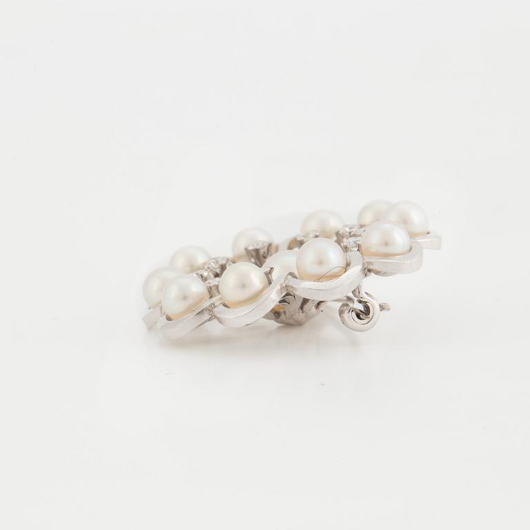 A brooch set with cultured pearls and round, brilliant-cut diamonds.