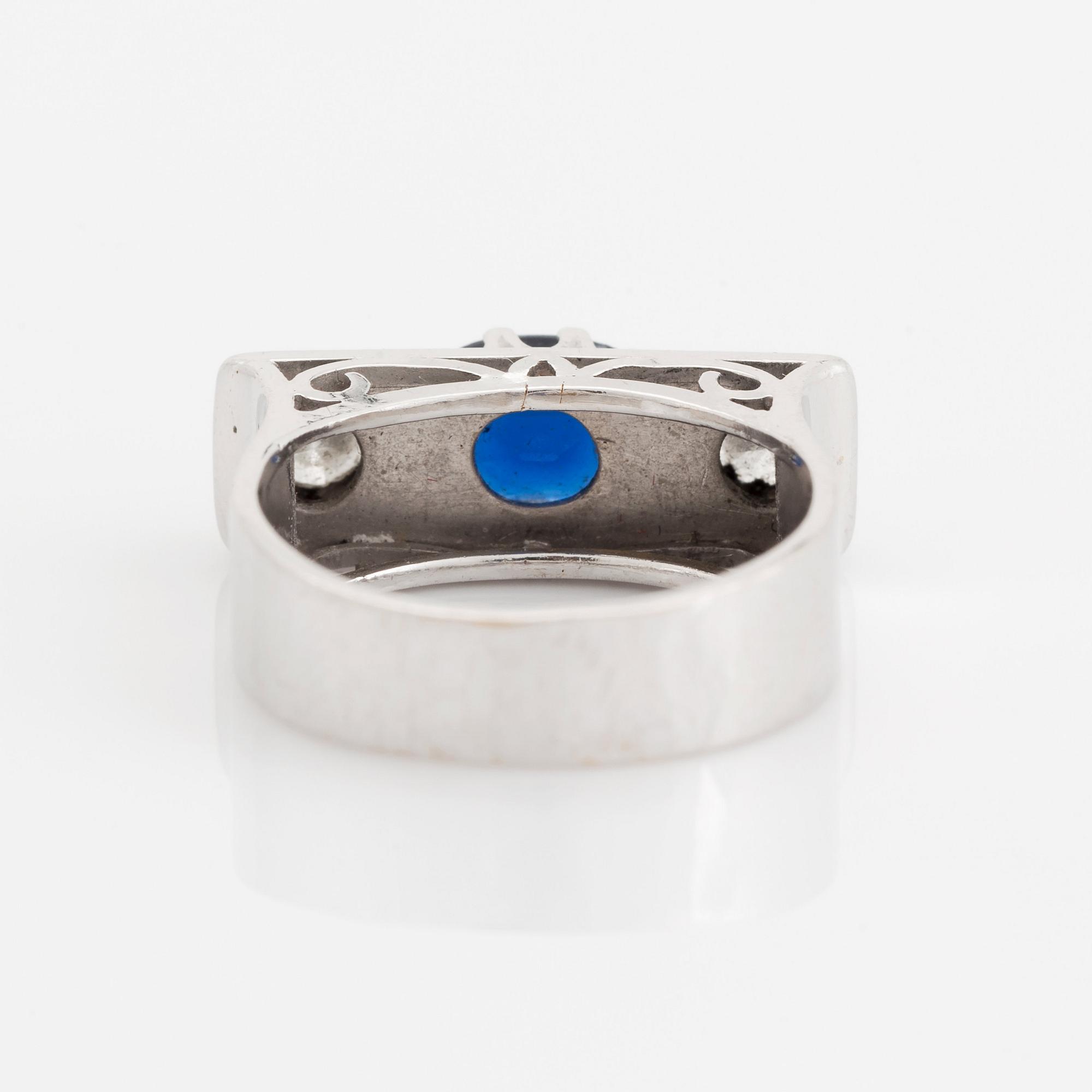 An 18K white gold ring set with a faceted sapphire, possibly synthetic, and round brilliant-cut diamonds.