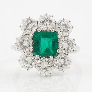 An 18K whitegold ring set with a step-cut emerald and round brilliant-cut diamonds.