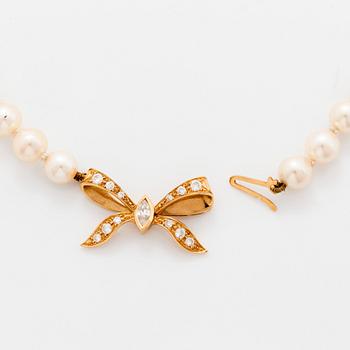 A cultured pearl necklace with a bow clasp in 18K gold set with round brilliant-cut diamonds.