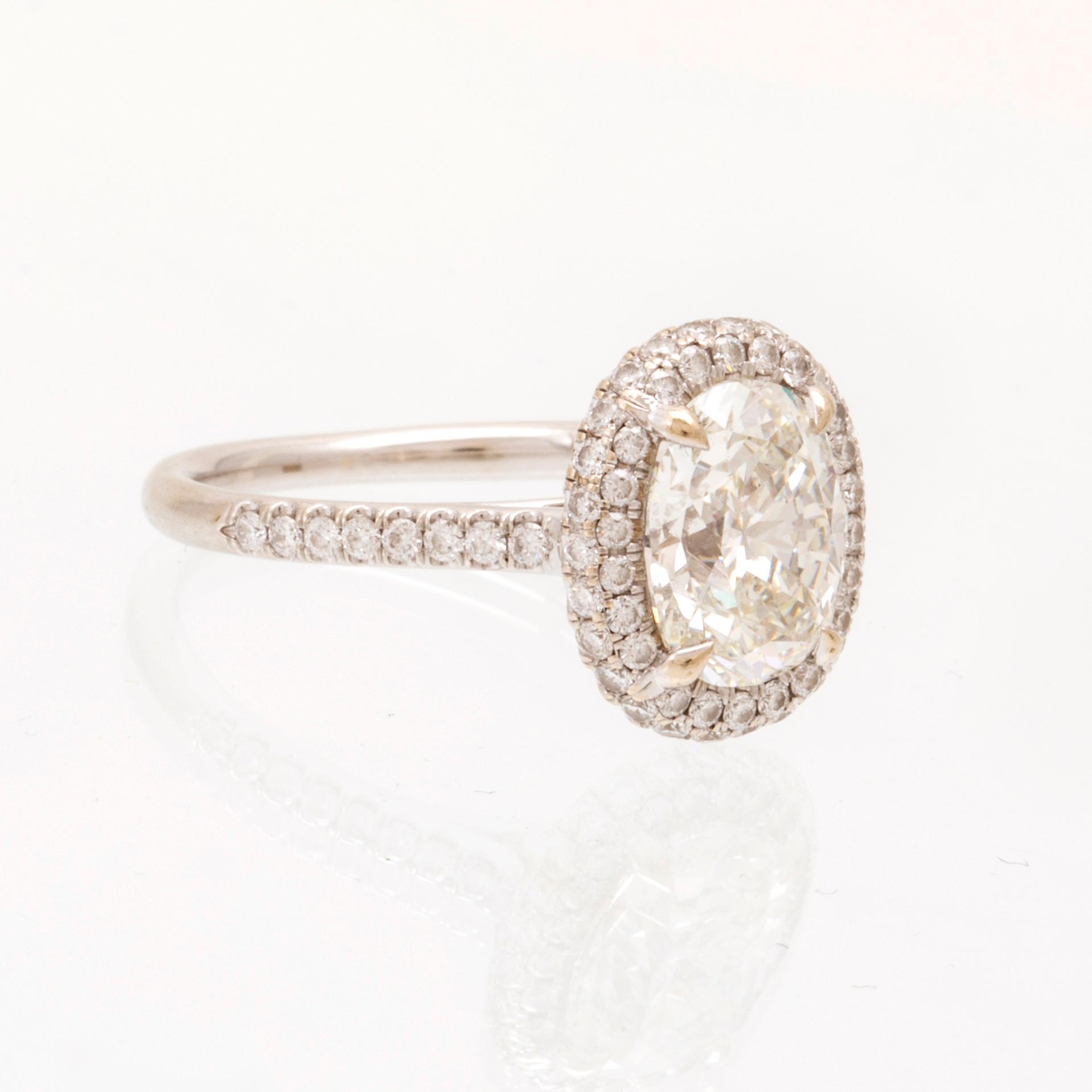 An 18K white gold ring by James Allen, set with an oval brilliant cut diamond in a halo of round brilliant cut diamonds.
