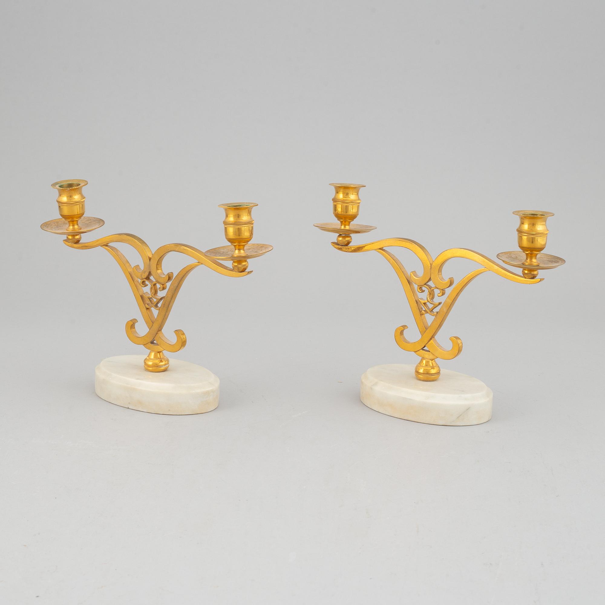 A pair of brass candle sticks om marble stands from the middle of 20th century.