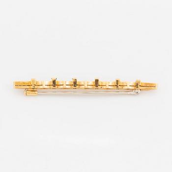 An 18K gold brooch set with step-cut emeralds and round brilliant-cut diamonds.
