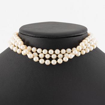 A three strand cultured pearl necklace, clasp in 18K gold with white stones and emeralds.