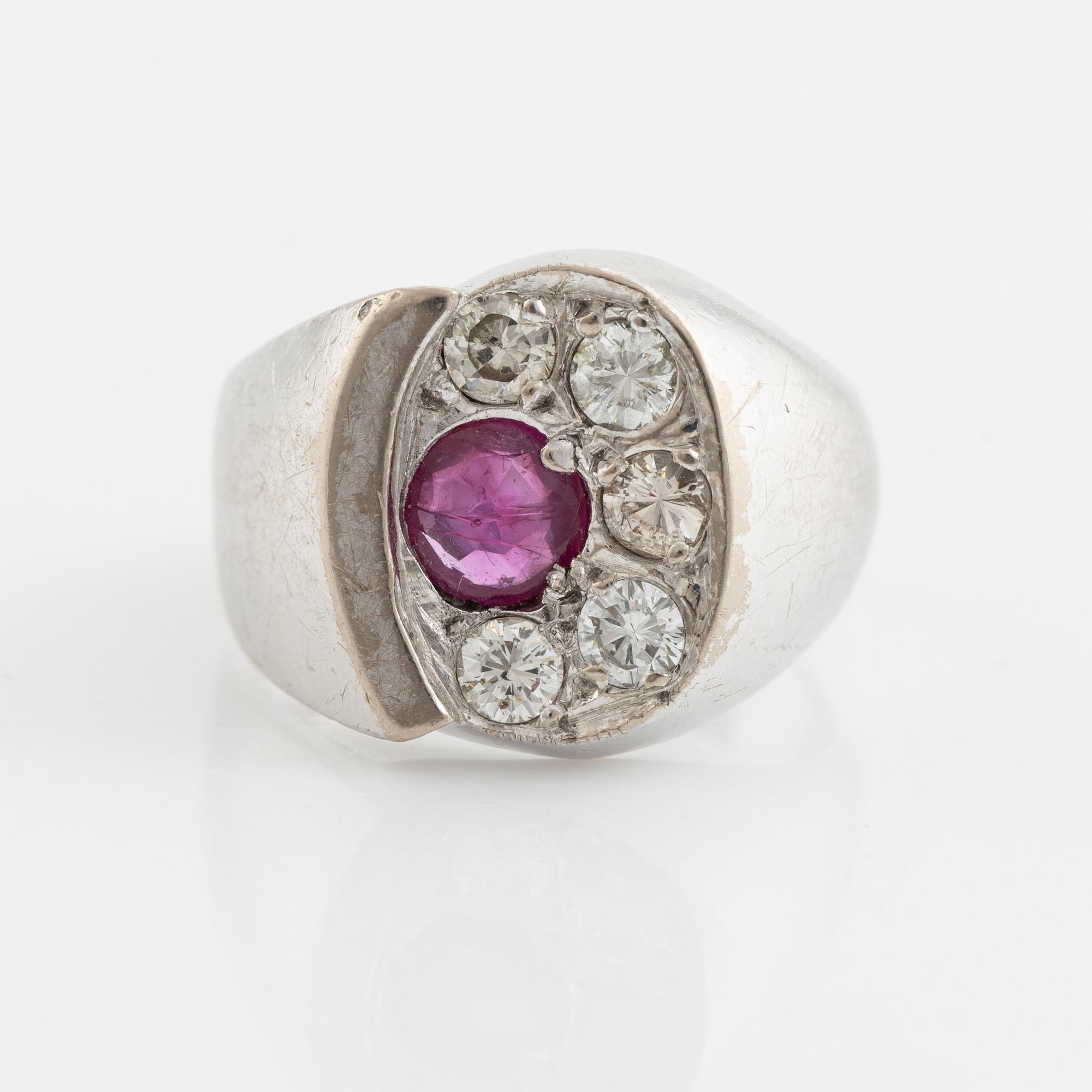 An 18K white gold ring set with a faceted ruby and round brilliant-cut diamonds.
