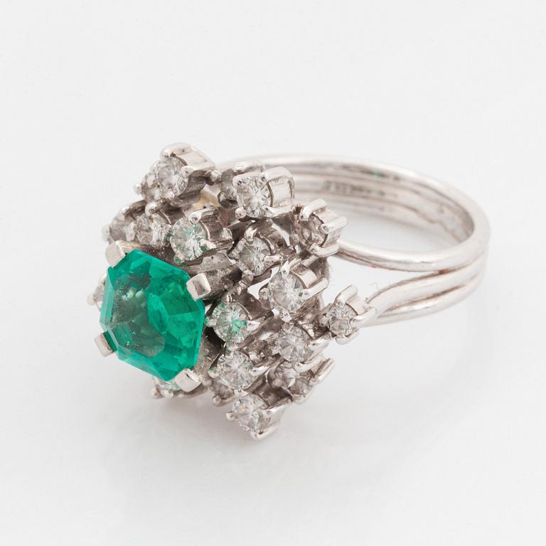 A platinum ring set with a faceted emerald and round brilliant-cut diamonds.