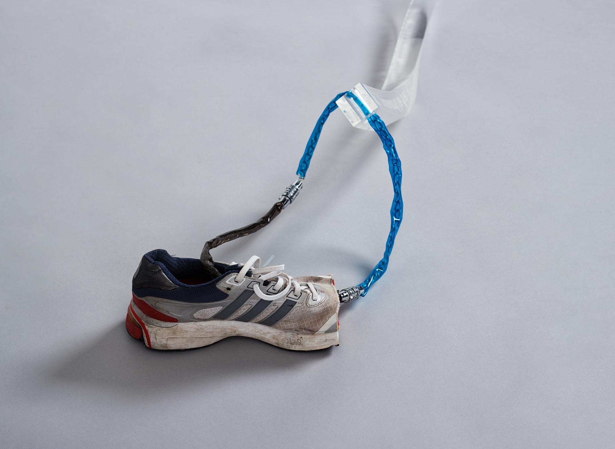 Yngve Holen, executed in 2014. Engraved acrylic glass, cable, lock, trainer, snap bracelet.