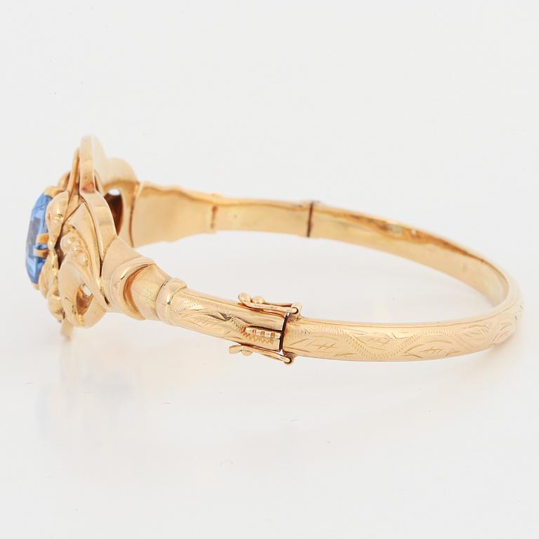 An 18K gold bangle set with a blue synthetic stone.