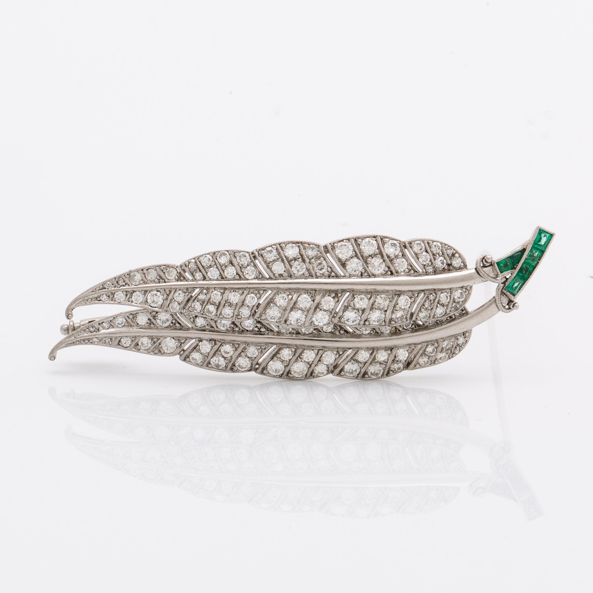 A platinum brooch set with round brilliant-cut diamonds and emeralds.