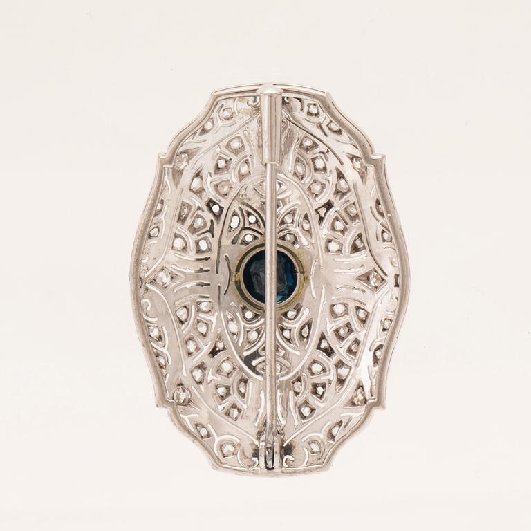 An 18K white gold brooch set with a facet-cut sapphire possibly synthetic, as well as brilliant and rose-cut diamonds.
