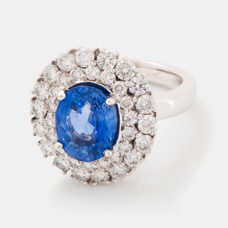 An 18K white gold ring set with an oval faceted sapphire and round brilliant-cut diamonds.