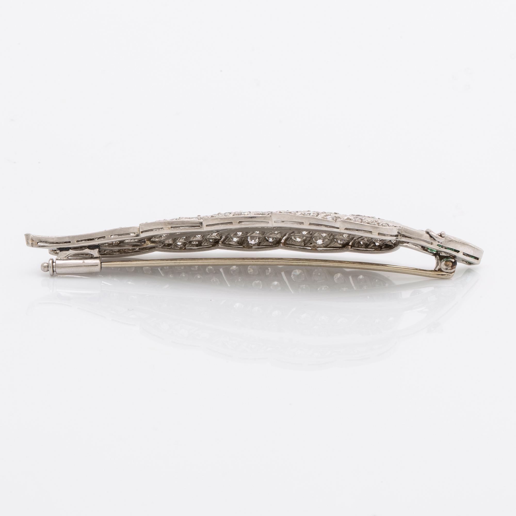 A platinum brooch set with round brilliant-cut diamonds and emeralds.