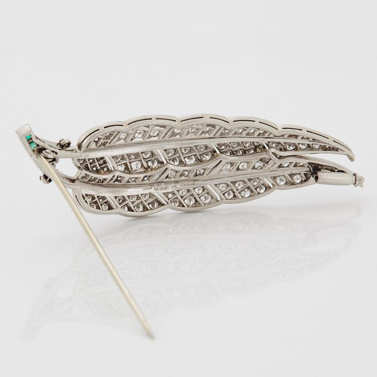 A platinum brooch set with round brilliant-cut diamonds and emeralds.