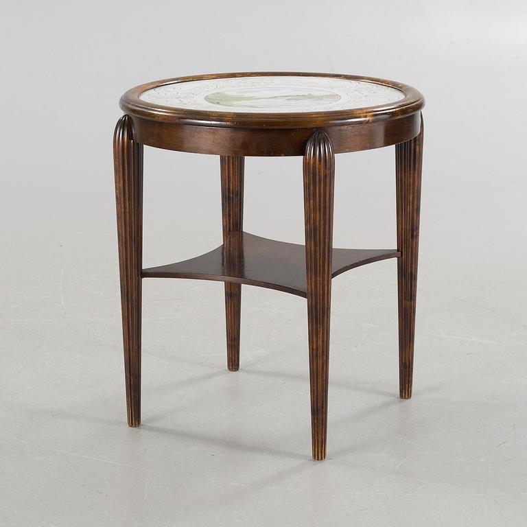 A table from the first halft of the 20th century with a "Kalmar Fajans" tabletop, painted by John Sjöstrand.
