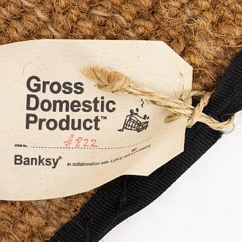 Banksy, dörrmatta, handbroderad med material från livvästar, 2019.