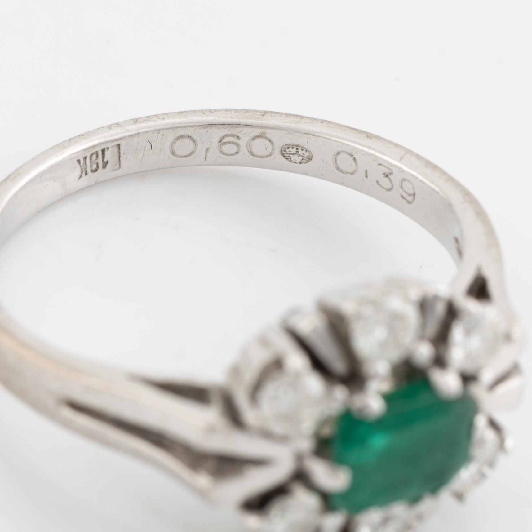 An 18K white gold ring set with a faceted emerald and round briliiant-cut diamonds.
