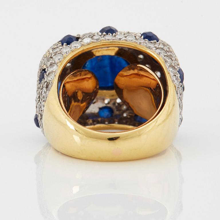 An 18K gold ring set with a cabochon-cut sapphire and round brilliant-cut diamonds and faceted sapphires.