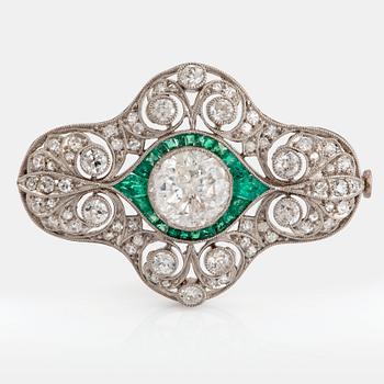 1147. A platinum brooch set with round brilliant- and old-cut diamonds and faceted emeralds.