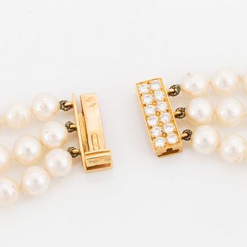 A Cartier triple strand cultured pearl necklace with an 18K gold clasp set with round brilliant-cut diamonds.