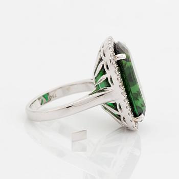 An 18K white gold ring set with a faceted green tourmaline and round brilliant-cut diamonds.