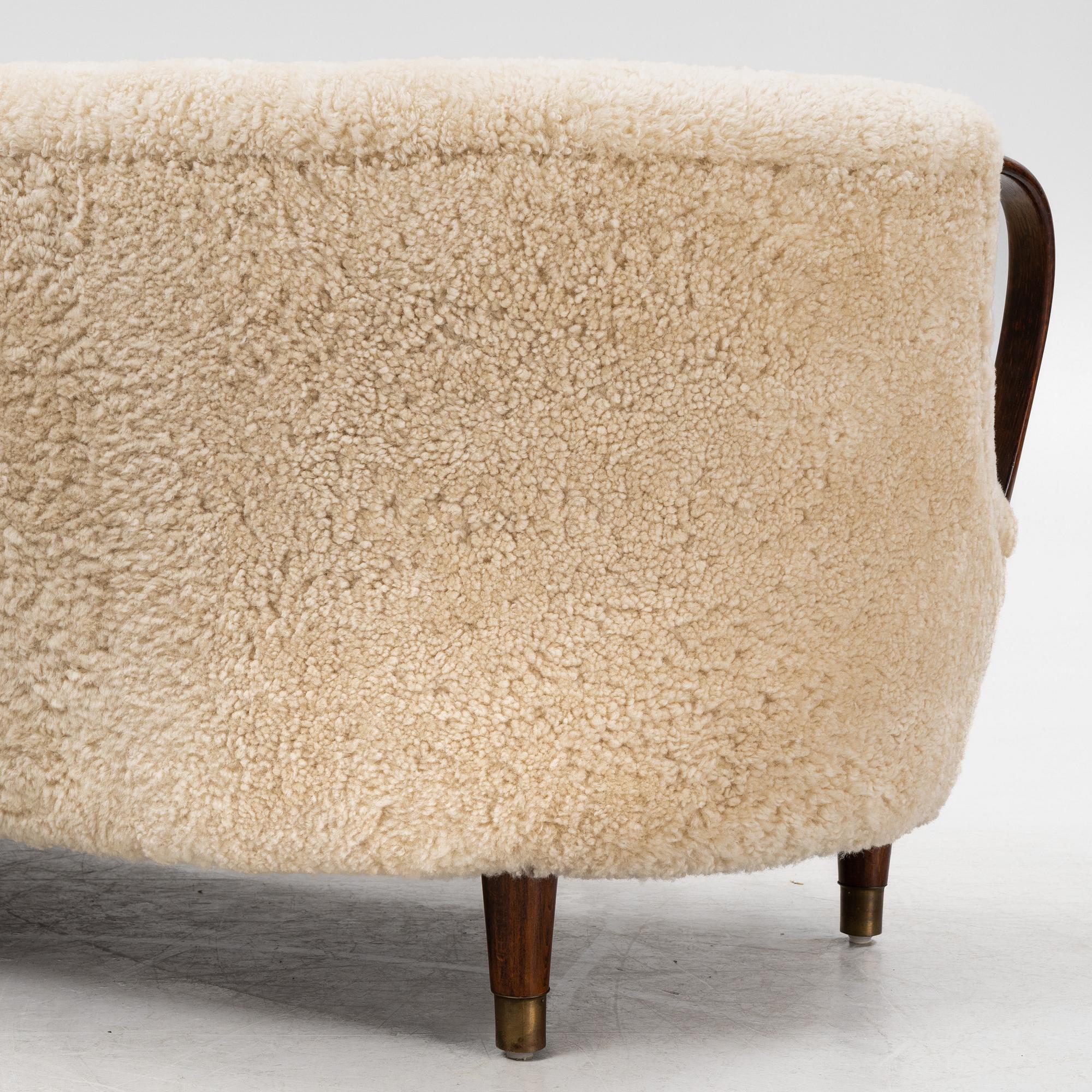 A curved sofa attributed to Viggo Boesen with new sheepskin upholstery and stained beech tree armrests.