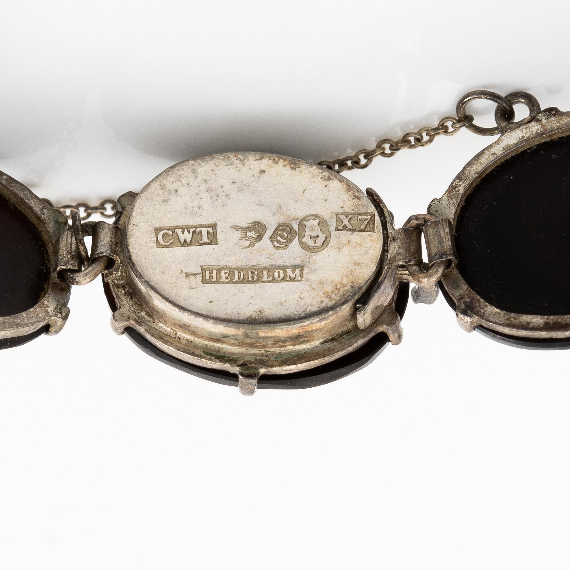 Samling smycken silver med svarta fasettslipade stenar, tre broscher, hattnål, medaljong och armband.