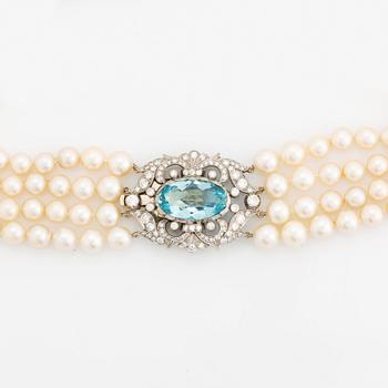 A four strand cultured pearl necklace with a clasp in 14K gold set with a faceted aquamarine.