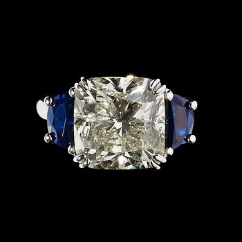 1107. RING, cushion cut diamant, 6.52 ct med blå safirer fattade på vardera sida.