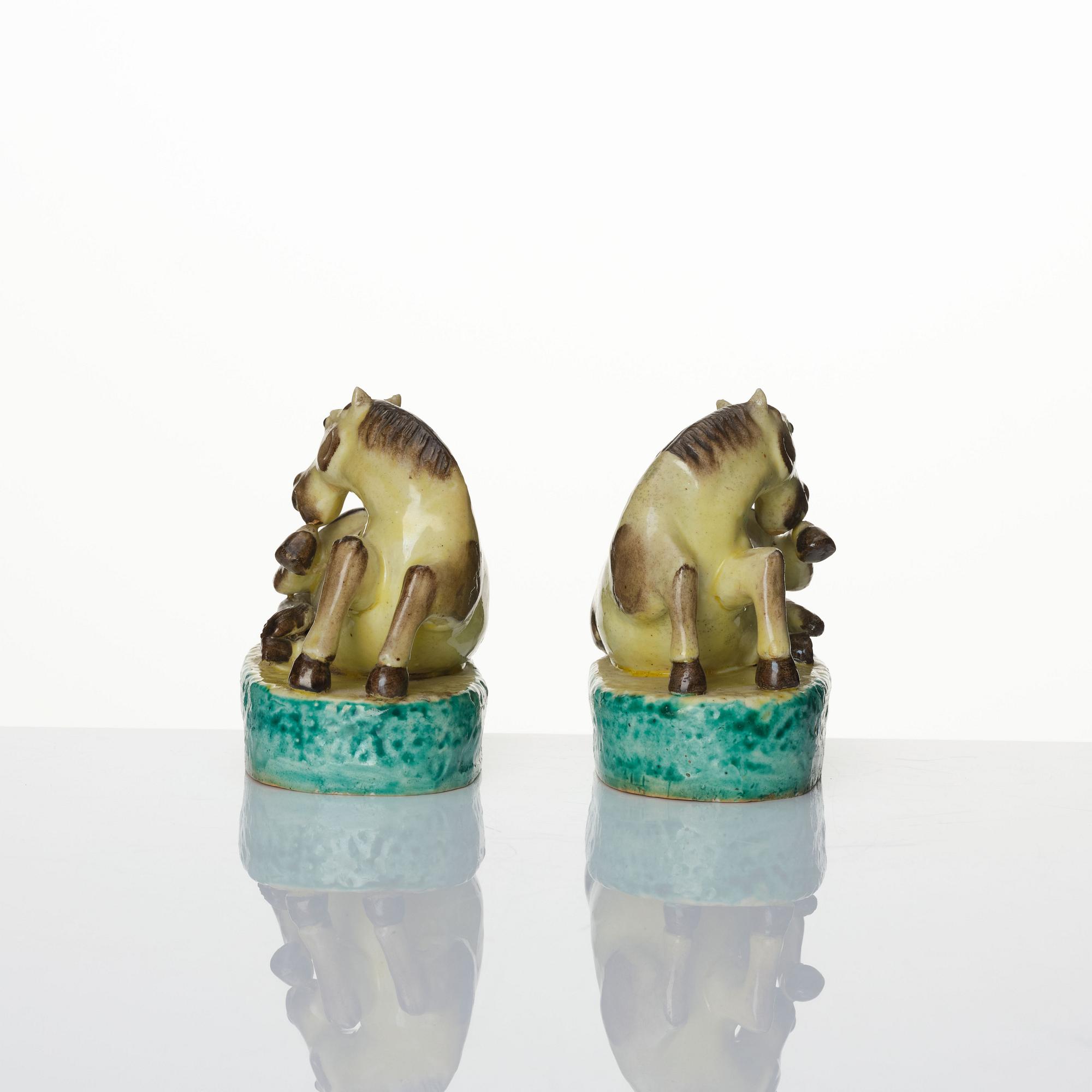 A pair of green, yellow and aubergine glazed biscuit figures of recumbent horses, Qing dynasty.