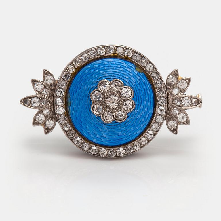 An palladium, silver and gold brooch with a metal pin, enamel decor and diamonds ca. 1.38 ct in total.