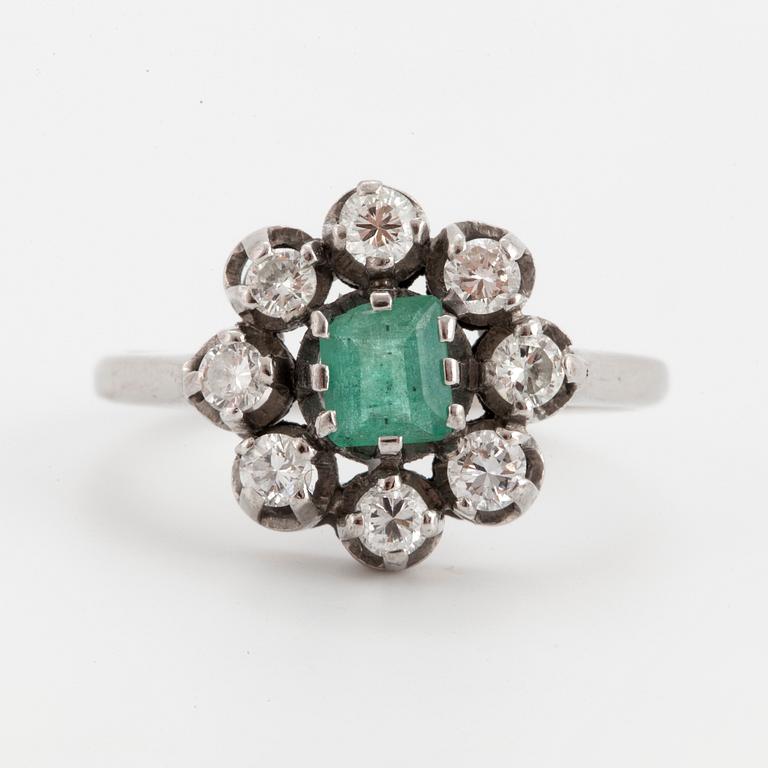 A ring set with a faceted emerald and round brilliant-cut diamonds.