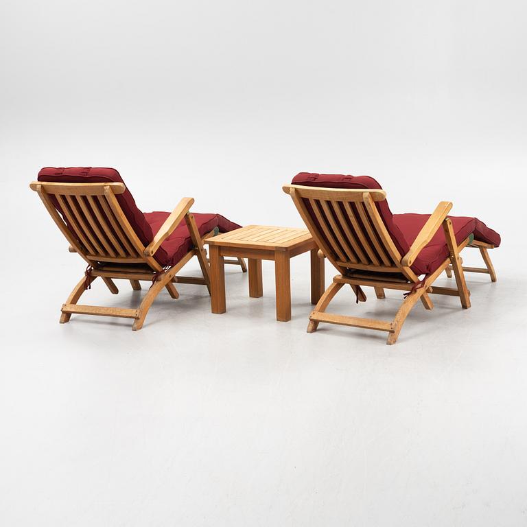A pair of teak deck chairs and a table, 21st Century.