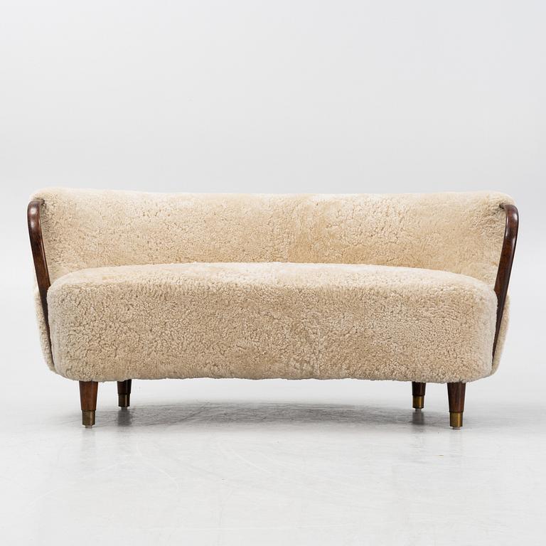 A curved sofa attributed to Viggo Boesen with new sheepskin upholstery and stained beech tree armrests.