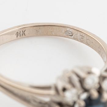 An 18K white gold ring set with a faceted sapphire and round brilliant-cut diamonds.