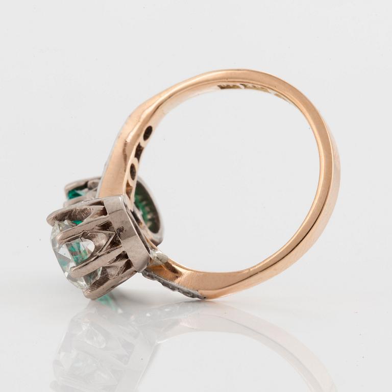 A CROSS-OVER RING set with an old-cut diamond and a round mixed-cut emerald.