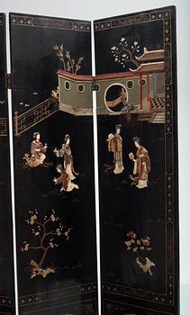 A chinese black lacquer six-panel screen, early 20th Century, with figures in gardens, inlays of carved mother of pearl, coloured bone, tree, and different stones. Back of panels with flowers painted in gold.