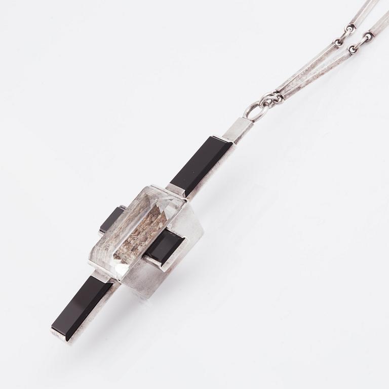 Wiwen Nilsson, hängsmycke i form av ett kors i sterlingsilver med fasettslipad bergkristall och onyx, Lund 1938.