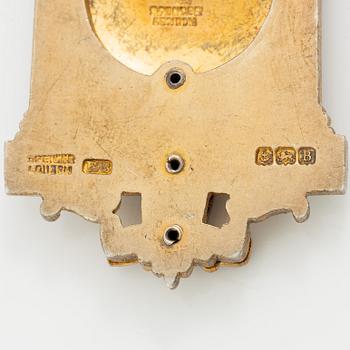 A jeton and pin, in gilded silver and 9 ct gold respectively.