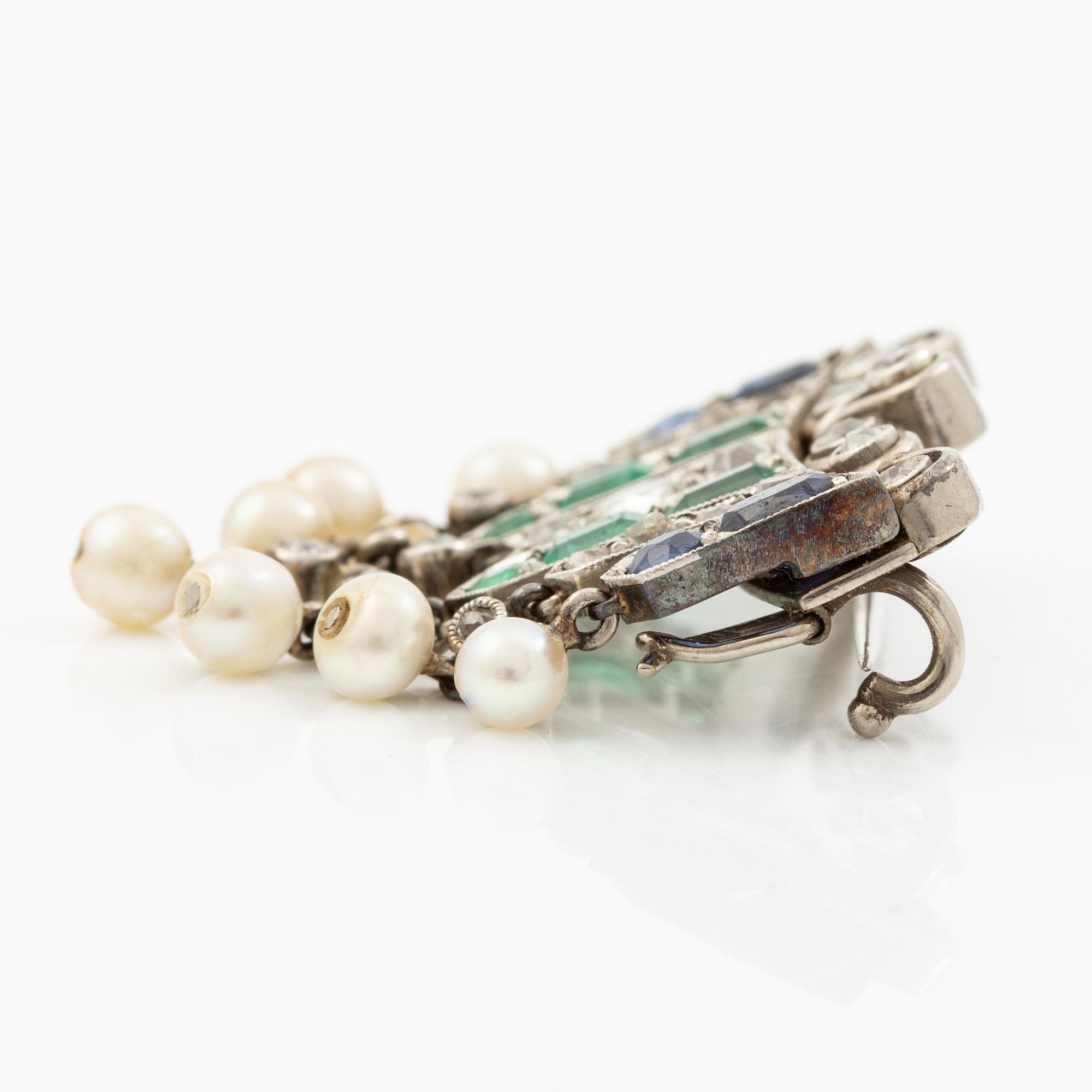 Brooch in platinum set with old-cut diamonds, sapphires, emeralds, and pearls.