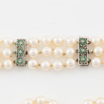 A three strand cultured pearl necklace, clasp in 18K gold with white stones and emeralds.
