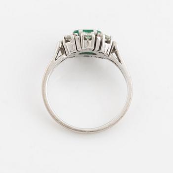 An 18K white gold ring set with a faceted emerald and round briliiant-cut diamonds.